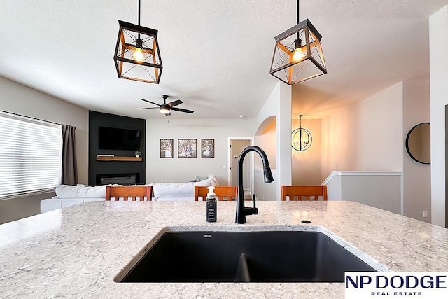 kitchen featuring light stone countertops, a sink, ceiling fan, and hanging light fixtures