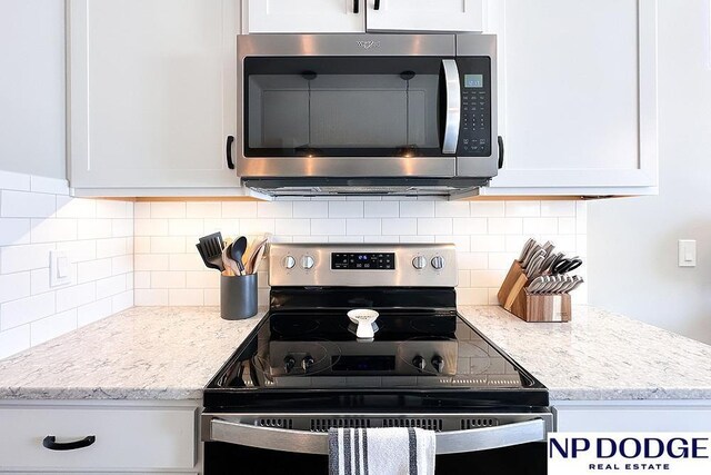 kitchen with decorative backsplash, appliances with stainless steel finishes, light stone counters, and white cabinetry