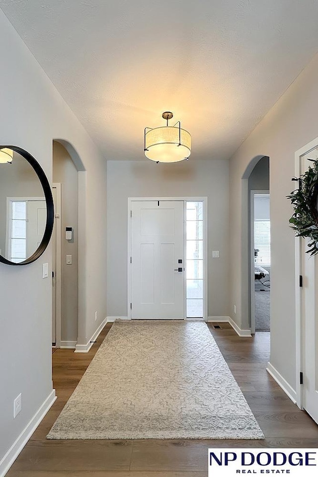 entrance foyer with arched walkways, dark wood finished floors, and a healthy amount of sunlight