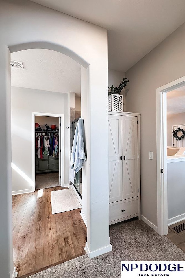 hallway featuring baseboards, wood finished floors, visible vents, and arched walkways