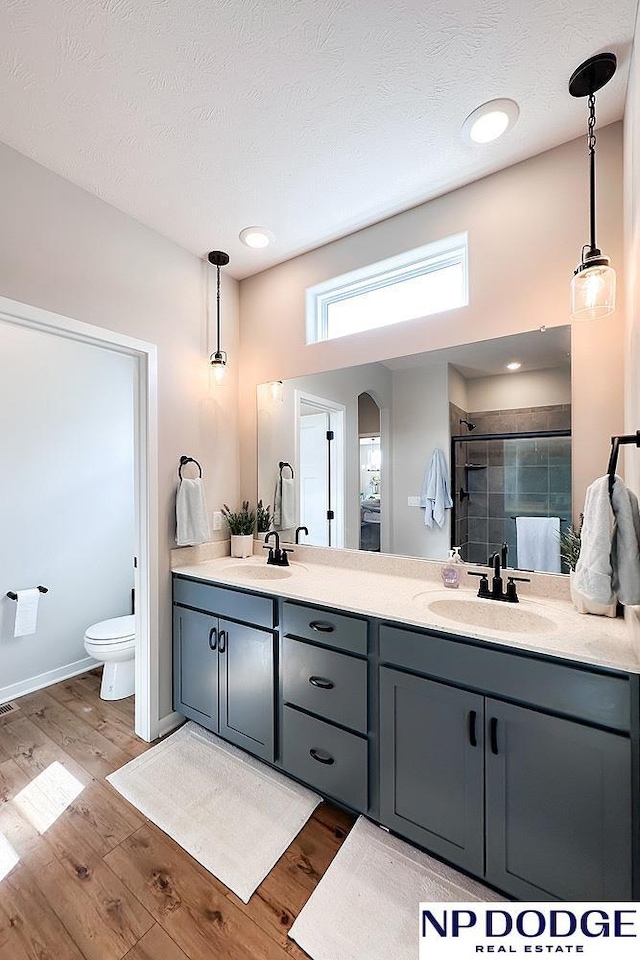 bathroom with double vanity, wood finished floors, toilet, a sink, and a stall shower