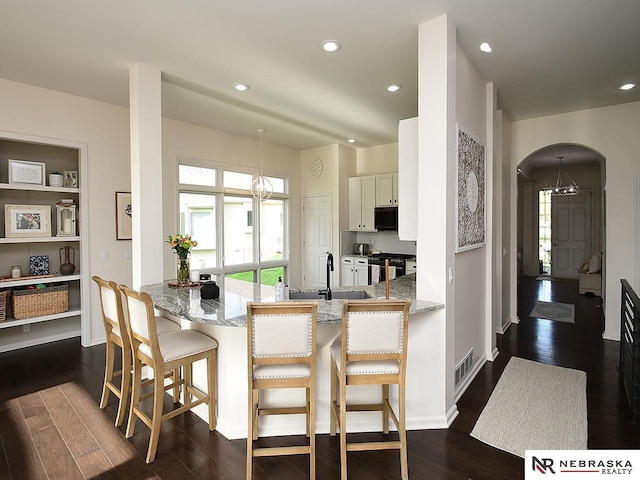 kitchen featuring black microwave, arched walkways, a notable chandelier, and gas range