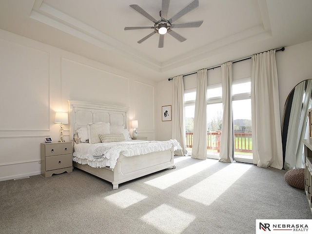 bedroom featuring ceiling fan, access to outside, a tray ceiling, and carpet
