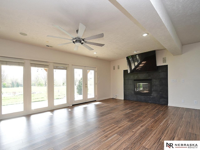unfurnished living room with wood finished floors, a textured ceiling, ceiling fan, a tile fireplace, and visible vents