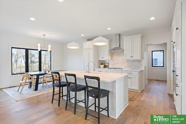 kitchen featuring light countertops, a healthy amount of sunlight, a sink, wall chimney exhaust hood, and gas stovetop