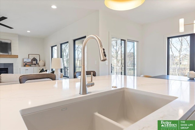 kitchen featuring recessed lighting, light stone counters, a large fireplace, a sink, and open floor plan