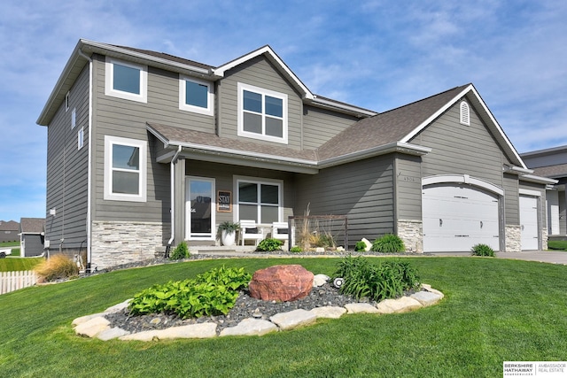 craftsman-style house with covered porch, driveway, a front yard, a garage, and stone siding