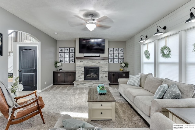 living area featuring baseboards, carpet flooring, ceiling fan, and a stone fireplace