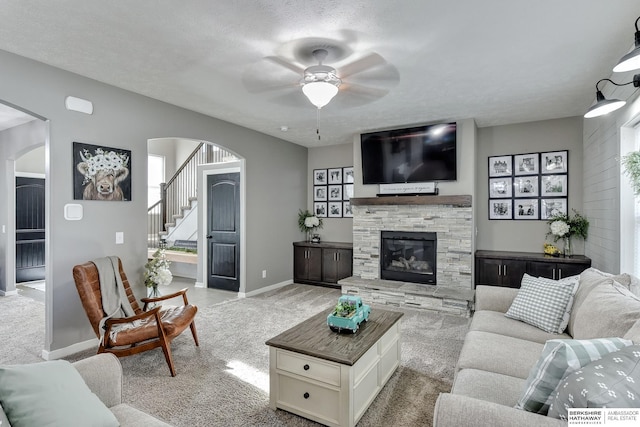 living room featuring light colored carpet, a fireplace, arched walkways, stairs, and a ceiling fan