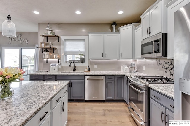kitchen with gray cabinets, tasteful backsplash, a sink, light wood finished floors, and appliances with stainless steel finishes