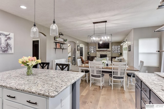 kitchen featuring a kitchen island, a stone fireplace, arched walkways, light stone countertops, and light wood-style flooring