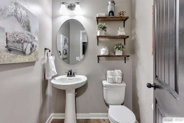 half bath featuring a sink, baseboards, toilet, and wood finished floors