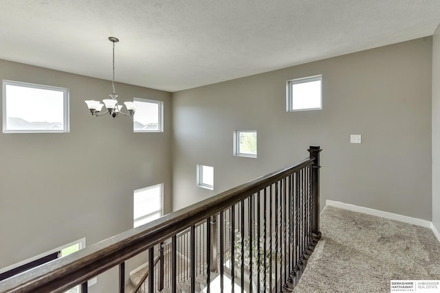 hallway with baseboards, a chandelier, carpet, and an upstairs landing