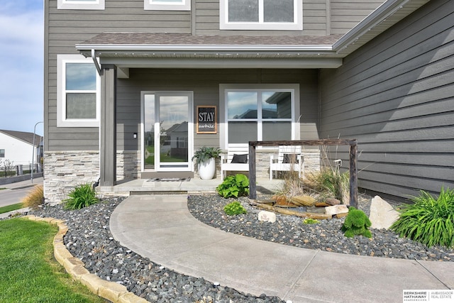 entrance to property with a shingled roof and stone siding