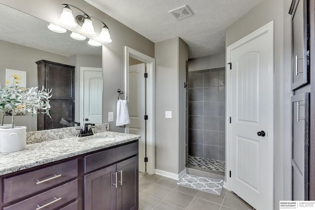 bathroom featuring tile patterned flooring, vanity, a textured ceiling, visible vents, and a stall shower