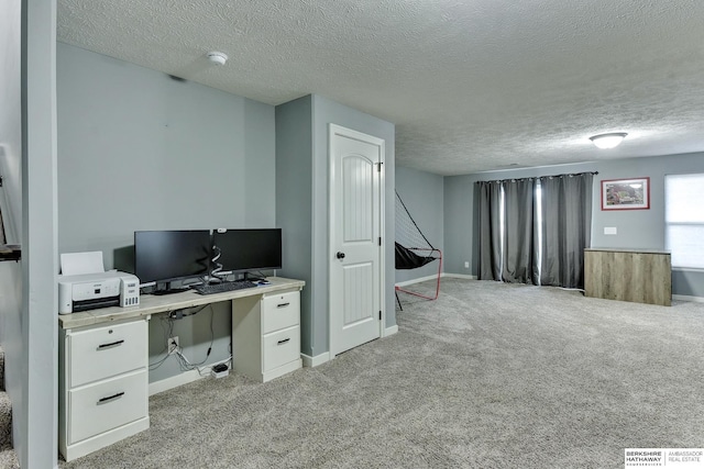 unfurnished office featuring baseboards, a textured ceiling, and light colored carpet
