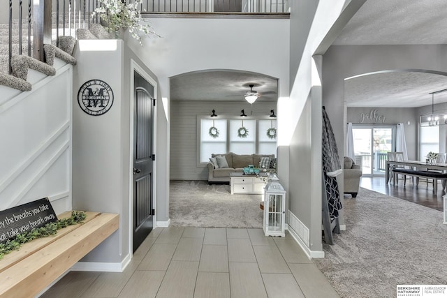 carpeted entryway with arched walkways, a textured ceiling, baseboards, and ceiling fan with notable chandelier