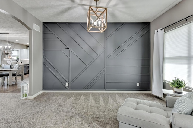carpeted dining space featuring an inviting chandelier, a decorative wall, arched walkways, baseboards, and visible vents