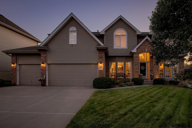 view of front of house featuring an attached garage, concrete driveway, a yard, and brick siding