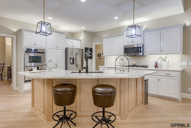 kitchen featuring stainless steel appliances, decorative backsplash, a sink, and light wood finished floors