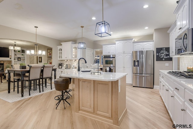 kitchen with a breakfast bar area, a sink, light wood finished floors, glass insert cabinets, and stainless steel appliances