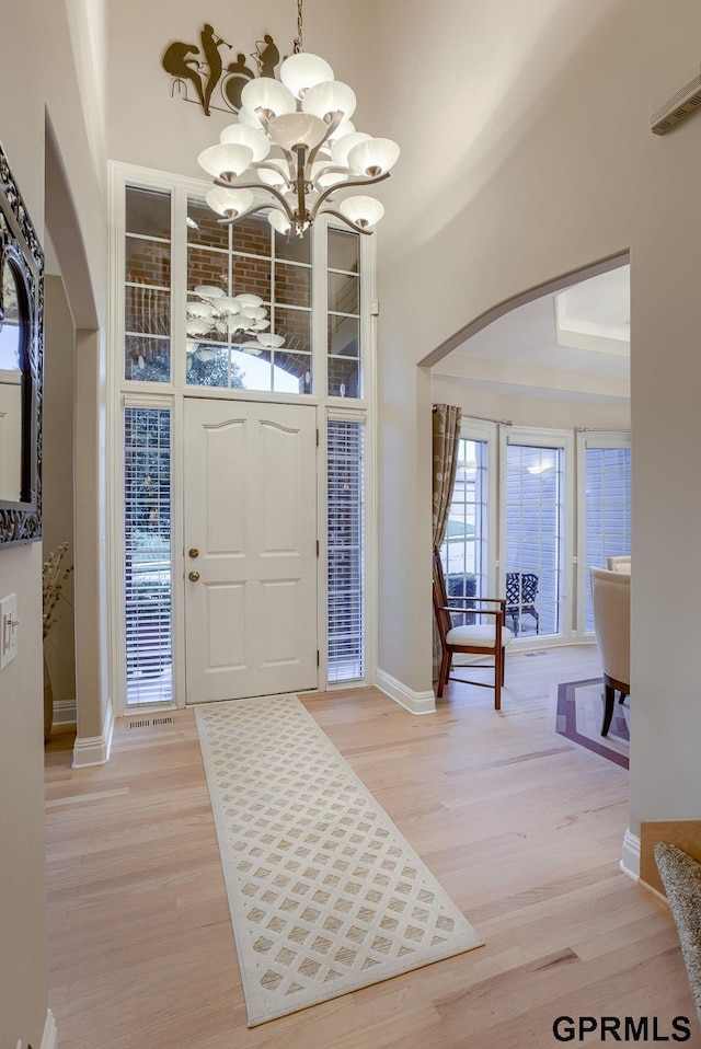 foyer featuring arched walkways, baseboards, a notable chandelier, and light wood-style floors
