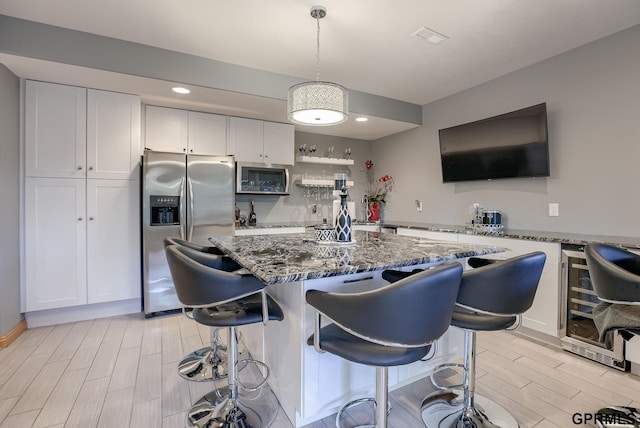 kitchen featuring a kitchen breakfast bar, wood finish floors, dark stone countertops, wine cooler, and stainless steel appliances