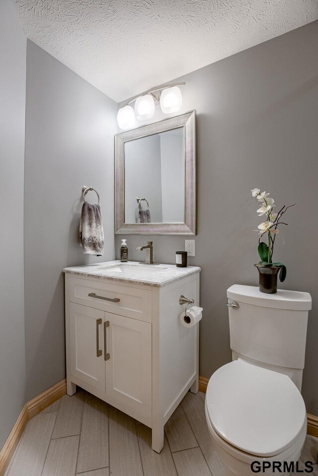 half bathroom with vanity, a textured ceiling, baseboards, and toilet