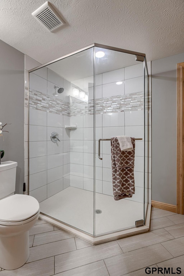 full bathroom featuring toilet, a textured ceiling, visible vents, and a shower stall