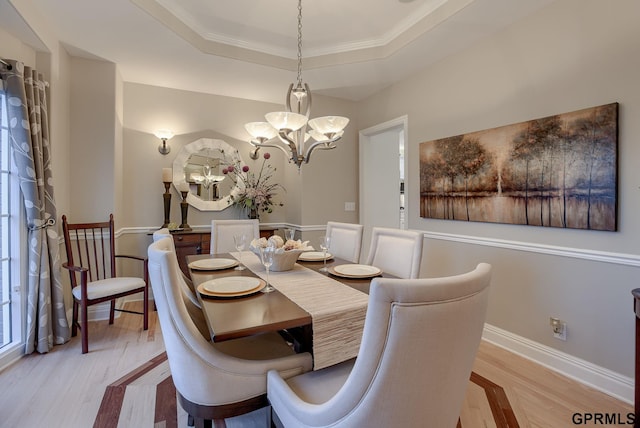 dining area featuring a raised ceiling, baseboards, an inviting chandelier, and light wood finished floors