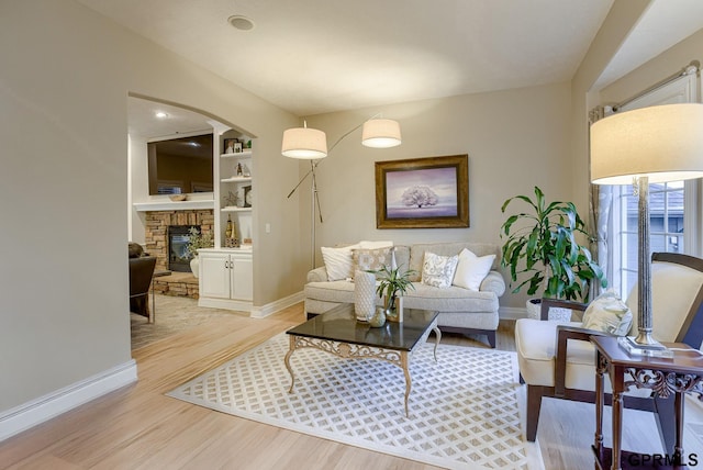 living area featuring built in features, baseboards, a stone fireplace, and light wood-style flooring
