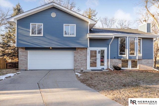 split level home featuring concrete driveway, a chimney, brick siding, and a garage