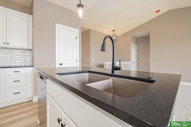 kitchen with vaulted ceiling, dark stone countertops, a sink, pendant lighting, and white cabinetry