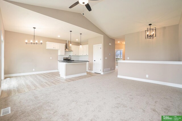 unfurnished living room with a sink, baseboards, visible vents, lofted ceiling, and ceiling fan with notable chandelier
