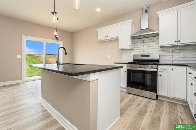 kitchen featuring stainless steel range with gas cooktop, dark countertops, a sink, light wood-style flooring, and wall chimney exhaust hood