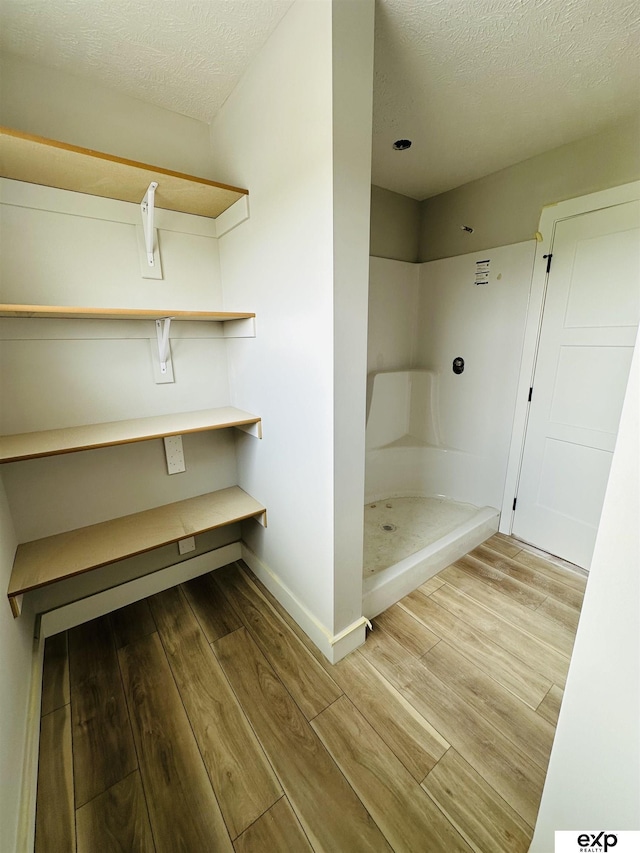 bathroom featuring baseboards, wood finished floors, a textured ceiling, and a shower stall