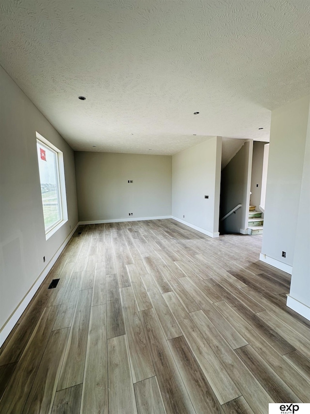unfurnished living room featuring wood finished floors, a textured ceiling, baseboards, and stairway