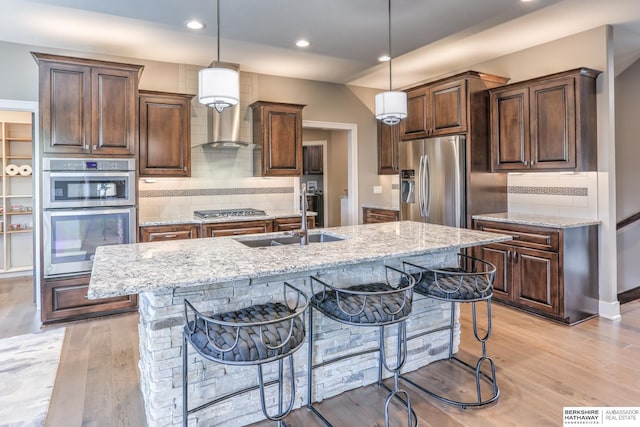 kitchen featuring a kitchen breakfast bar, light stone countertops, stainless steel appliances, and light wood finished floors