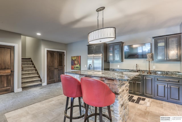kitchen with dark stone countertops, a center island, stainless steel fridge, glass insert cabinets, and a breakfast bar area