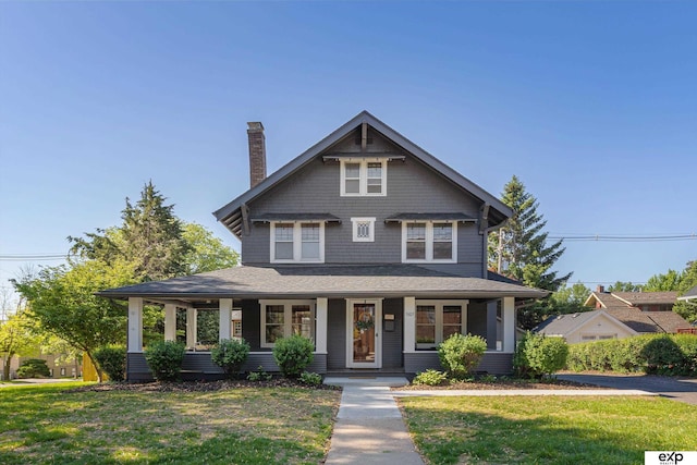view of front of house featuring a chimney, a porch, and a front yard
