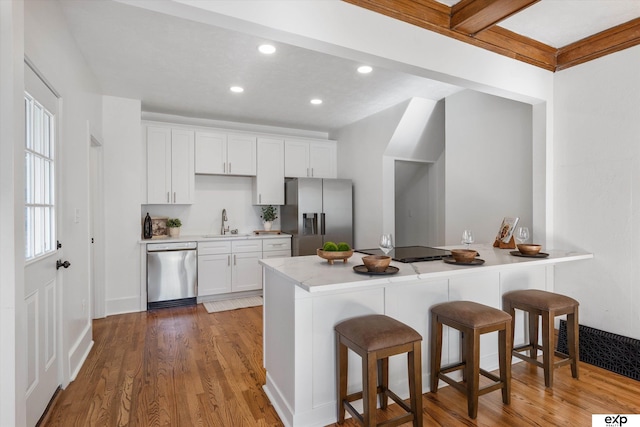 kitchen with appliances with stainless steel finishes, a sink, a breakfast bar, wood finished floors, and recessed lighting