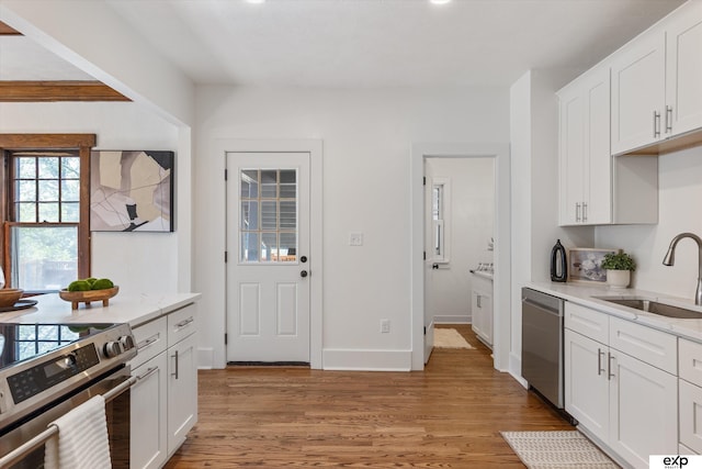 kitchen with a sink, appliances with stainless steel finishes, light wood finished floors, and white cabinets