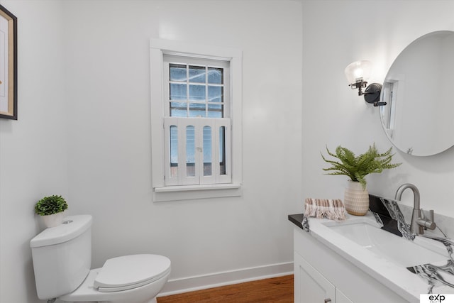half bathroom featuring wood finished floors, toilet, vanity, and baseboards