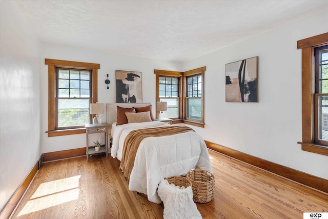 bedroom with multiple windows, light wood-style flooring, and baseboards