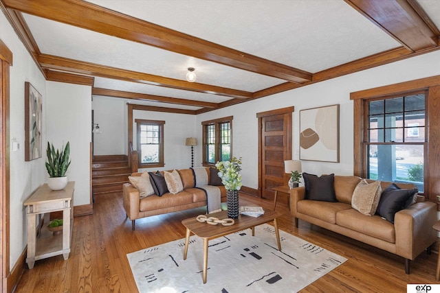 living room featuring light wood-type flooring, beam ceiling, baseboards, and stairway