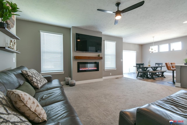 living area featuring baseboards, a textured ceiling, ceiling fan, and a glass covered fireplace