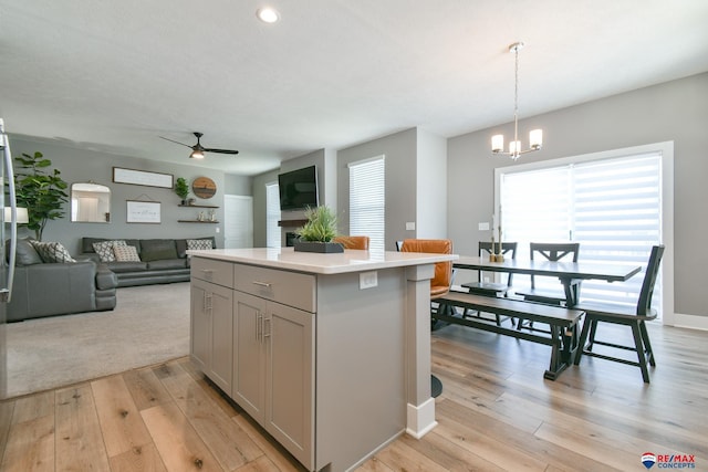 kitchen featuring open floor plan, a center island, light countertops, light wood-type flooring, and ceiling fan with notable chandelier