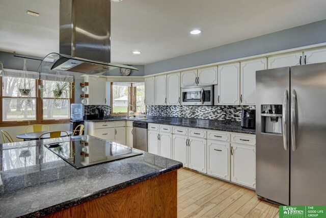 kitchen with white cabinets, island range hood, light wood-style floors, tasteful backsplash, and appliances with stainless steel finishes