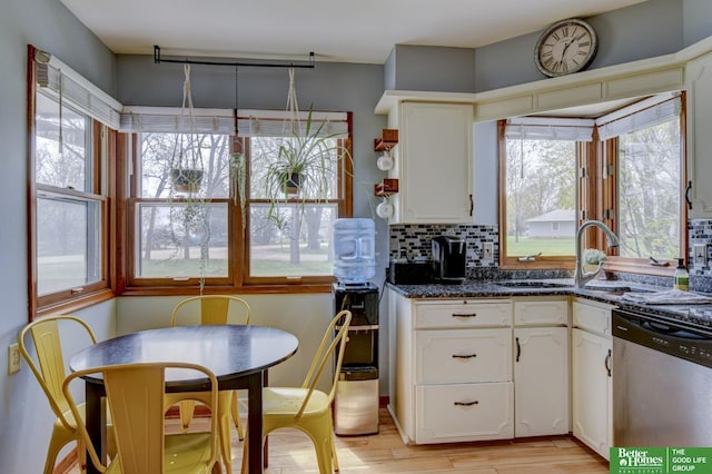 kitchen featuring stainless steel dishwasher, a sink, decorative backsplash, light wood finished floors, and white cabinetry