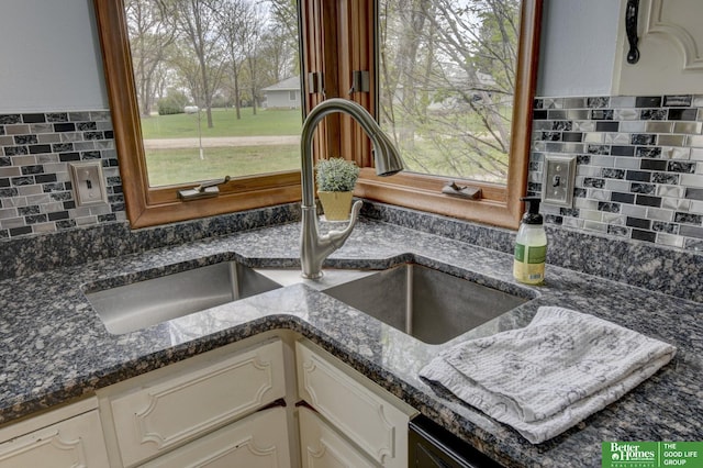 interior details with dark stone counters, decorative backsplash, white cabinetry, and a sink